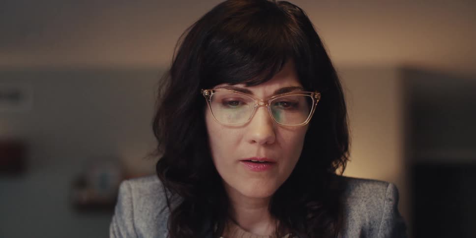 Woman working on a computer in her living room puts on her eyeglasses