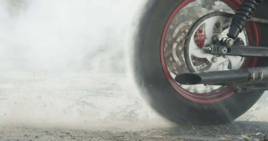Motorcycle wheel turning with smoke rising from ground