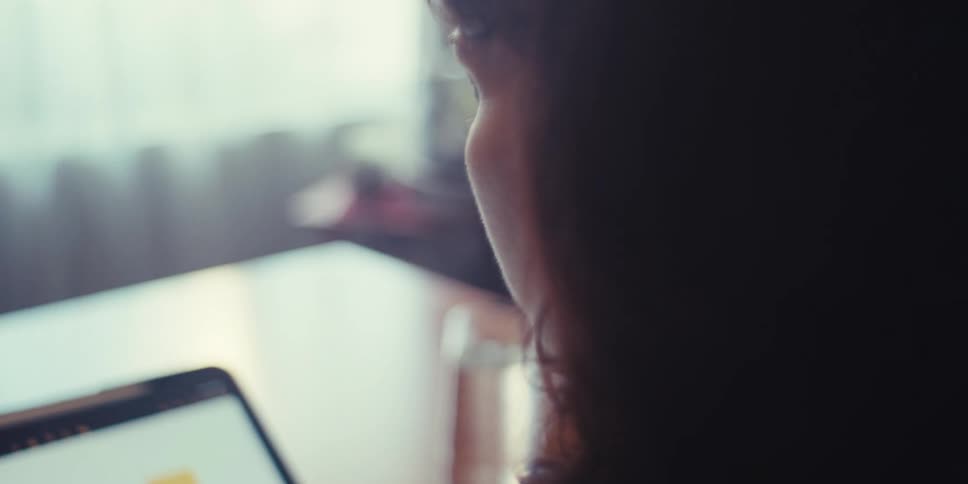 A woman views a colorful bar chart on a tablet screen seated at a desk in a softly lit room