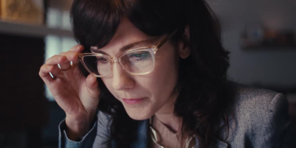 A young woman in her office wearing a blazer suit and glasses is working on her computer