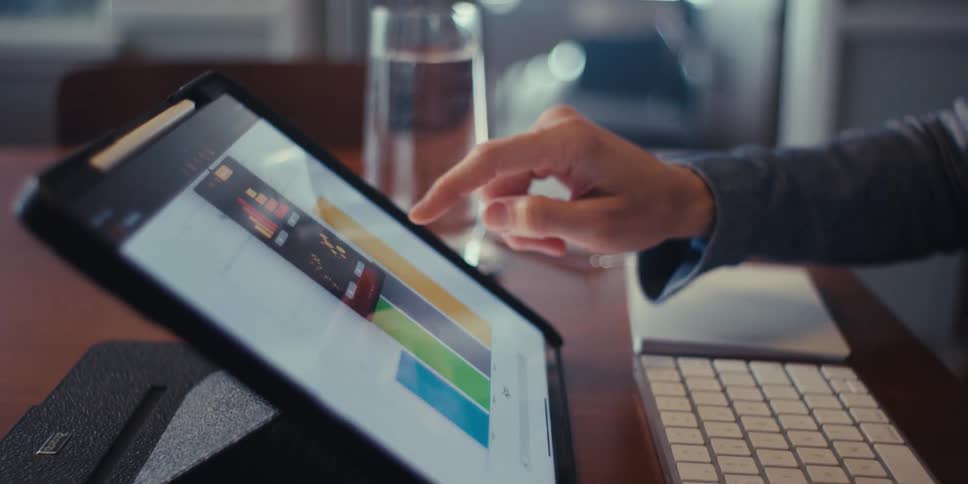 A woman is working on a tablet analyzing a colorful data chart or graph with her finger pointing at the screen