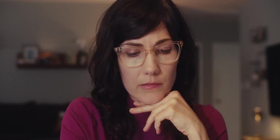 A woman adjusts her glasses while thinking