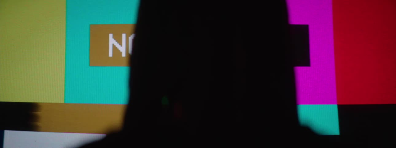 The silhouette of a person walking in front of a screen with several lines of different colors and text