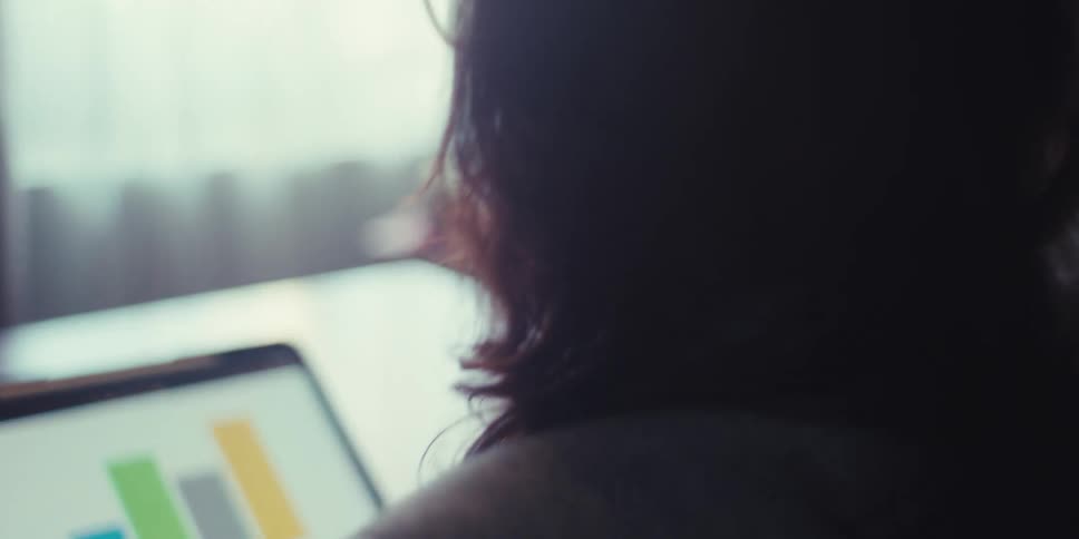 Woman sitting at a table looks at a graph displayed on a tablet during the daytime