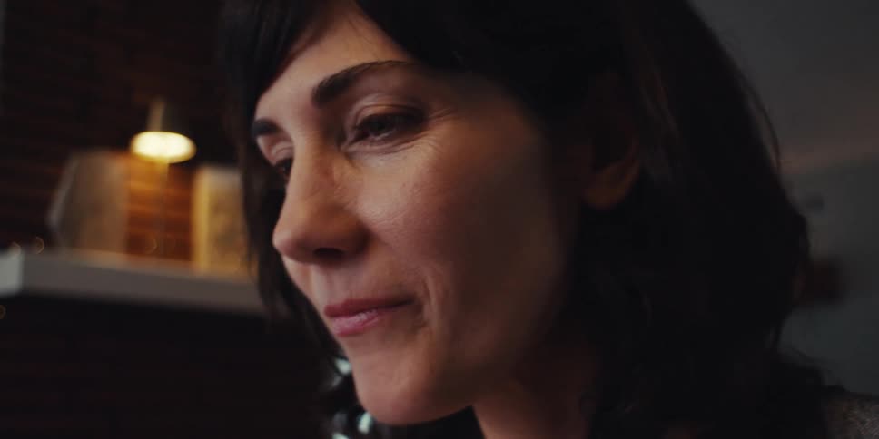 Woman smiles subtly as she holds her glasses close to her face