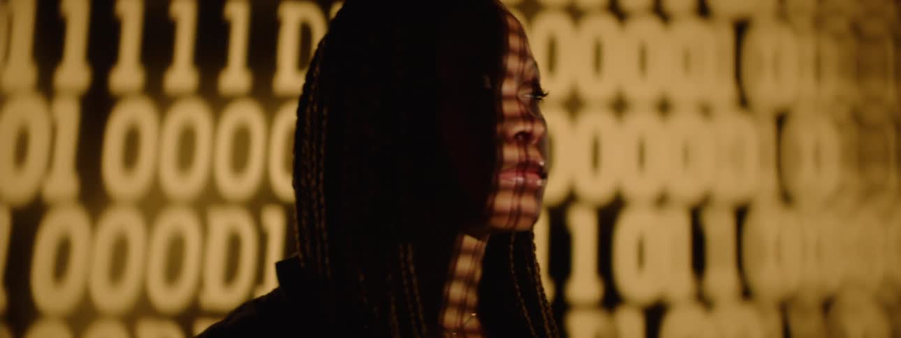 Woman interacting with a smartphone next to a large screen displaying a code of numbers