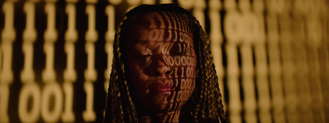 A tight shot of a womans face illuminated by projected binary code blending human expression with digital imagery