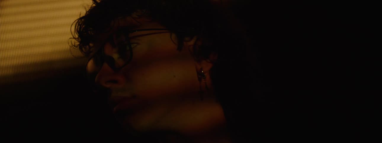 Silhouette of a curlyhaired man with glasses next to a screen displaying lights