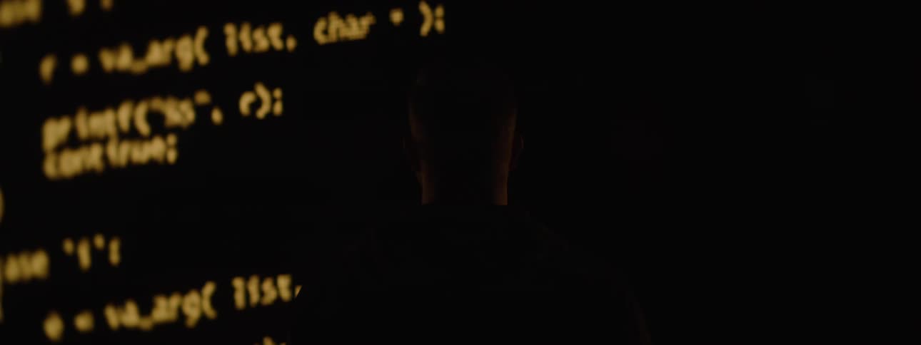 A person stands silhouetted against a glowing wall of code creating a dramatic techfocused atmosphere