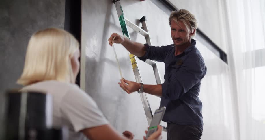 A man talks with a woman and puts tape on the wall