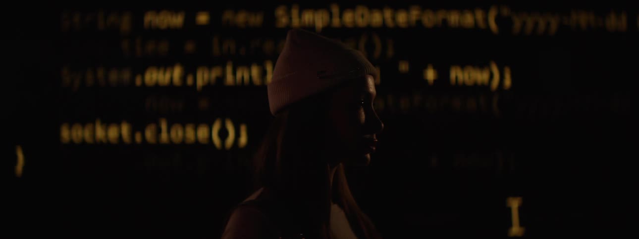 Computer code flashes on the wall behind the woman