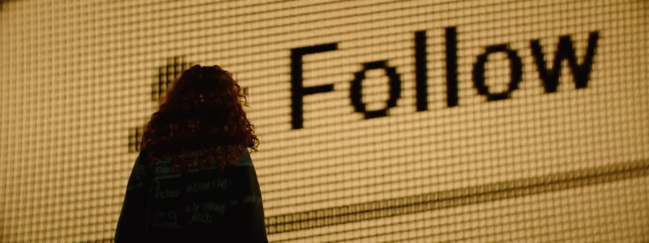 A woman watches a follow button being pressed on the projector display