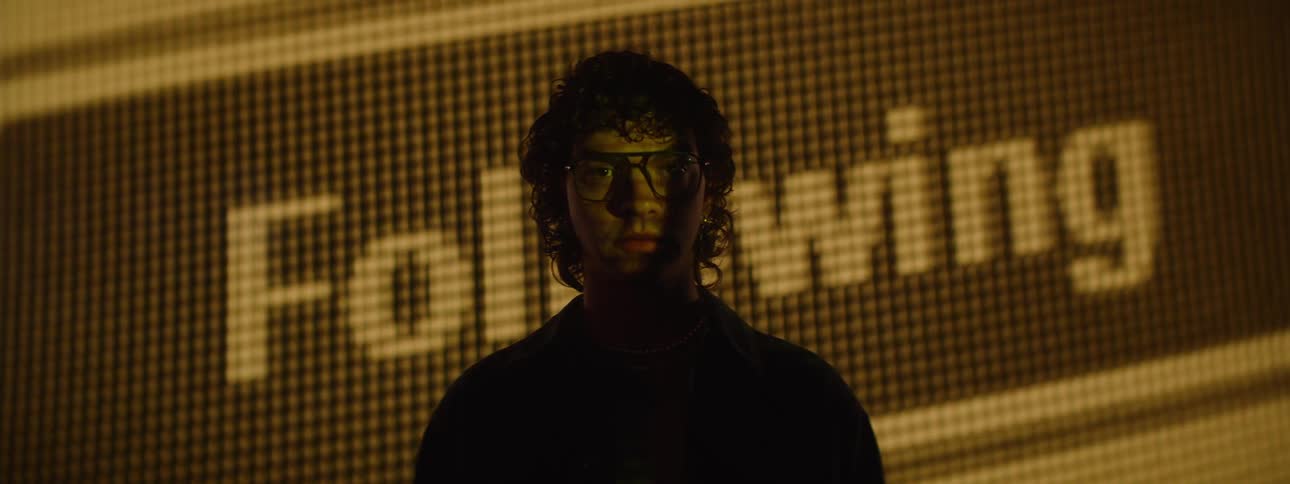 Young man with glasses facing a large digital screen