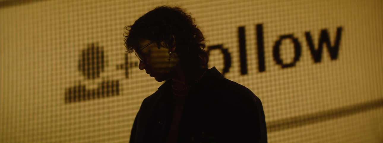 A person stands in front of a screen displaying a large follow button and a cursor pressing it