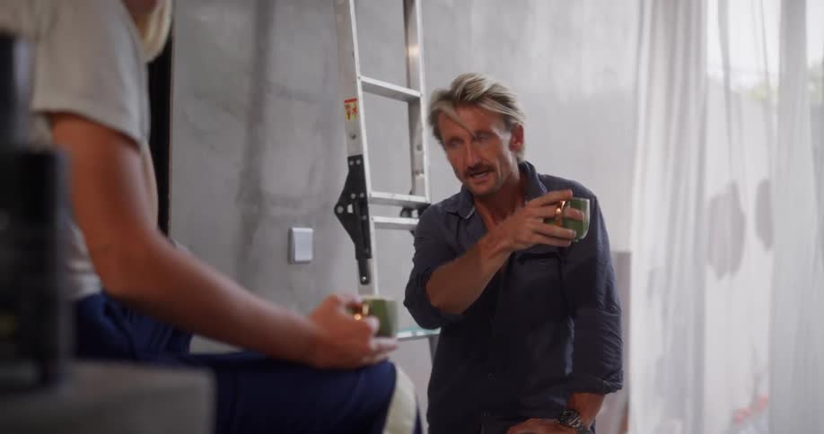 Man with a mug talking to another person who is sitting in front of him