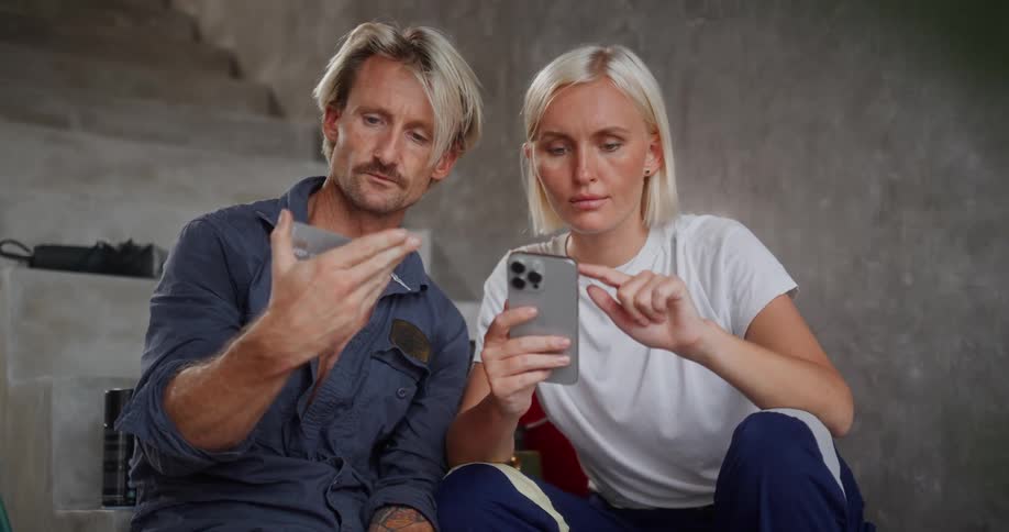 A man and woman are sitting on a staircase focused on making an online purchase together using a smartphone and credit card