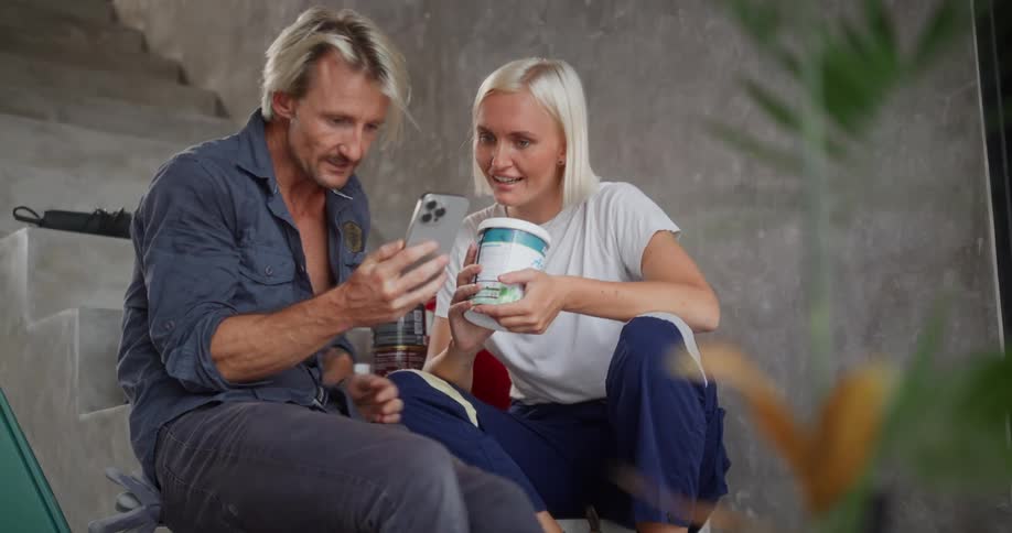 A man shows a cell phone to a woman and they laugh