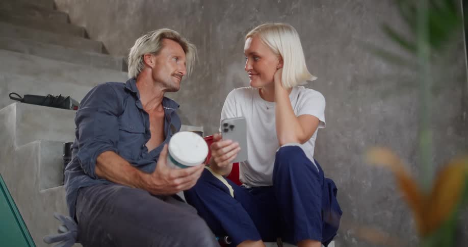 A man and a woman sitting on a staircase talking and then kissing the woman is holding a phone and the man is holding a container