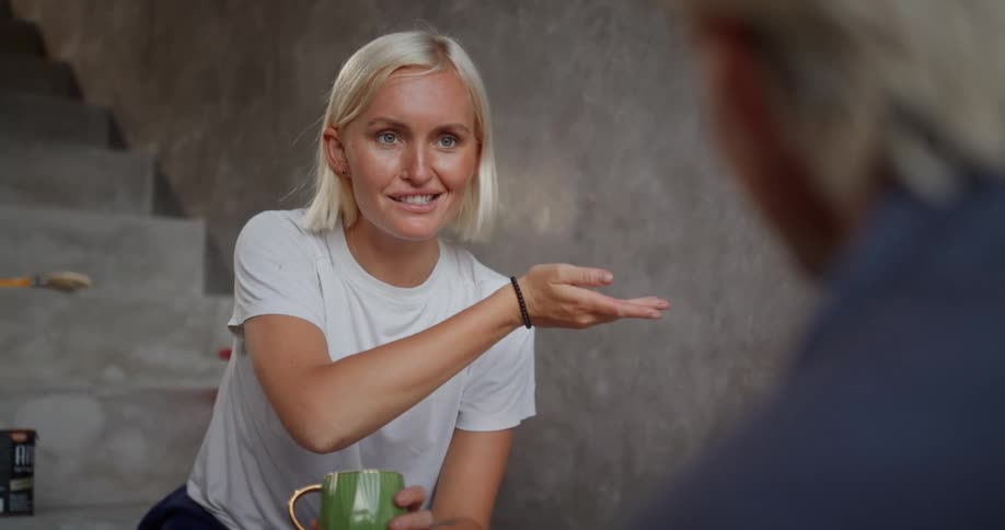 Woman sitting on stairs holding a cup and talking to a person in front of her