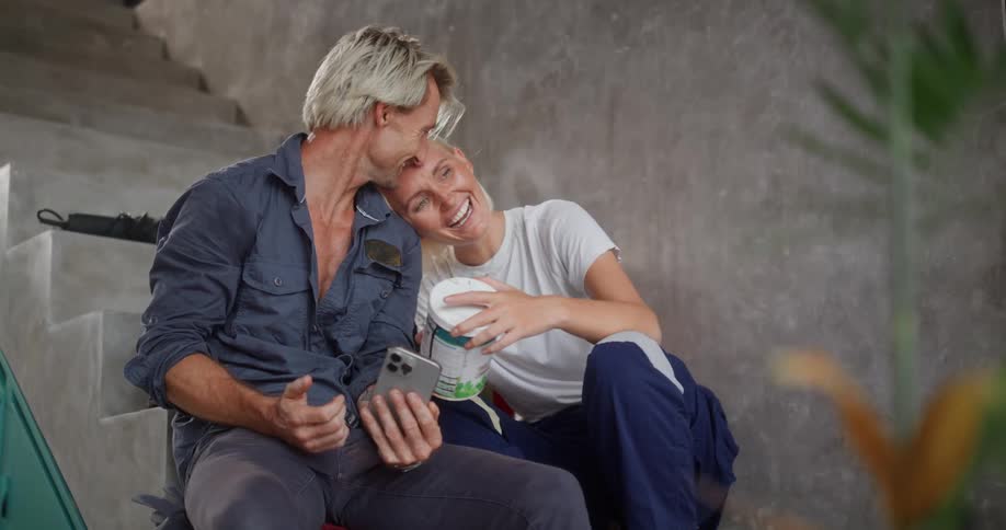 A man and woman are laughing while looking at a phone on the steps