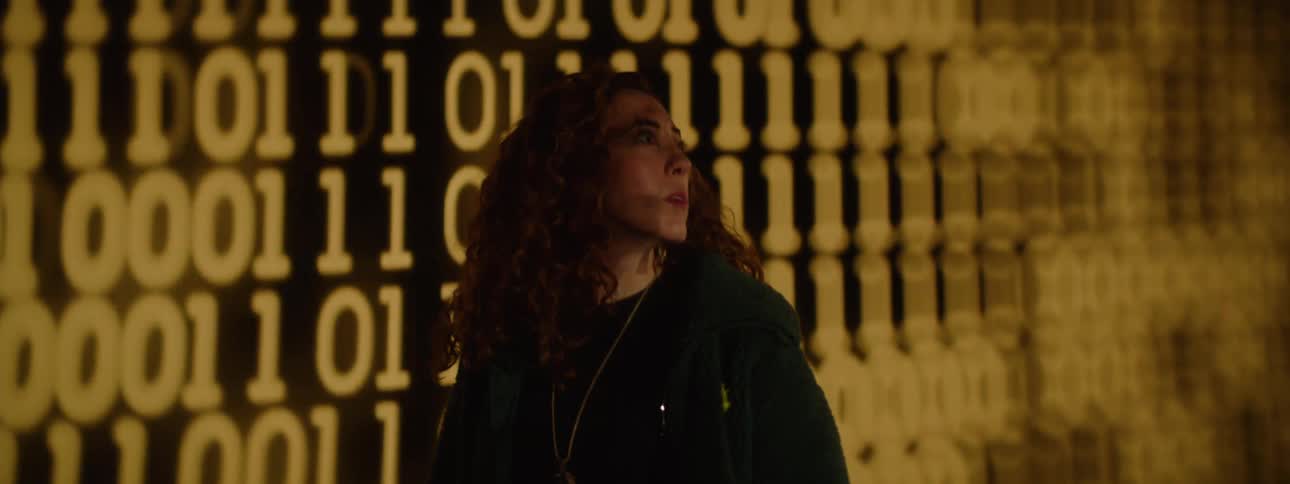 Woman near a large screen displaying binary numbers looking impressed as she observes her surroundings