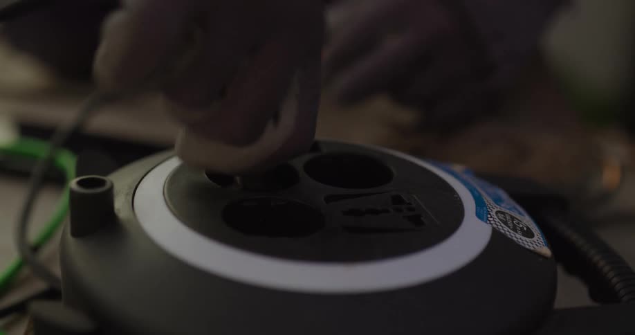 Person wearing gloves connects a cord and flips a switch on a machine