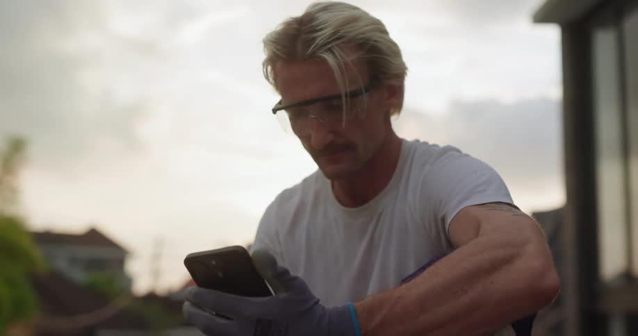 A technician installs a solar panel and checks data on his phone at sunset in a suburban area