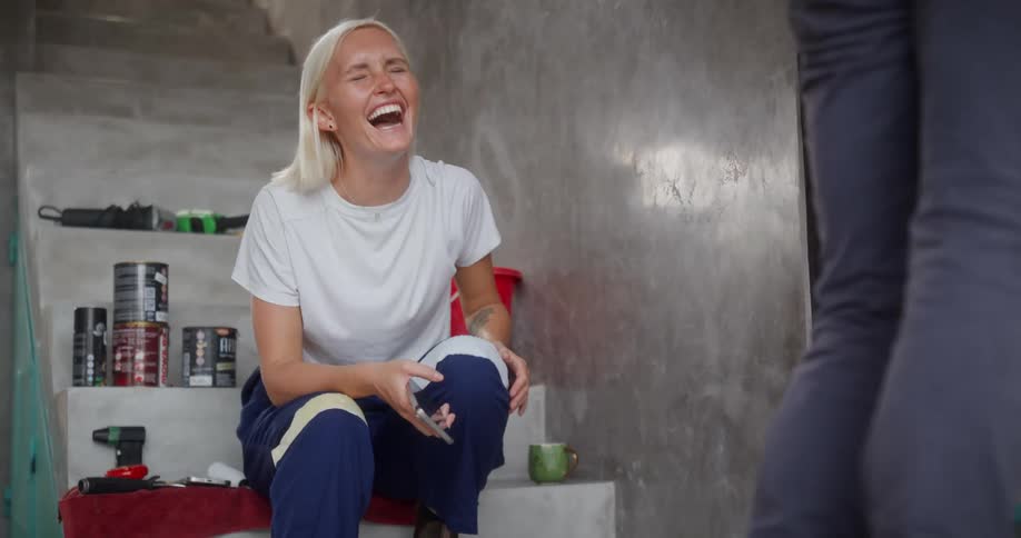 A smiling woman gestures toward a wall during what appears to be a home improvement or renovation project engaged in a friendly conversation
