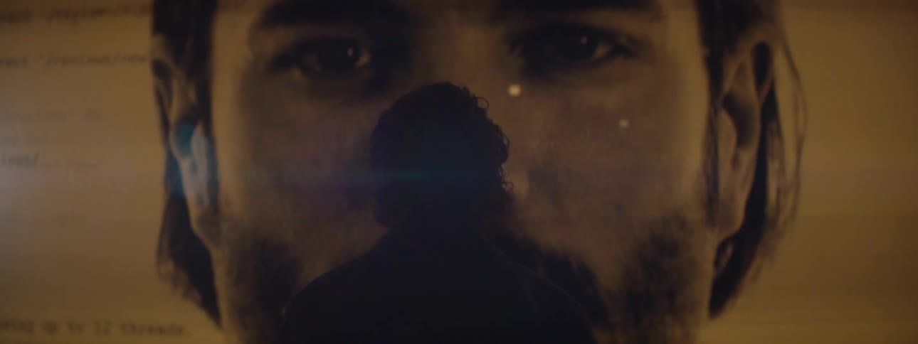 A silhouetted figure stands in front of a projection of code and a human face evoking themes of artificial intelligence and cybersecurity