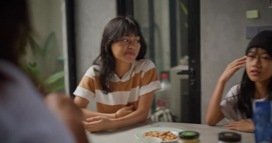 Three kids sit at a kitchen table casually talking in a relaxed home setting