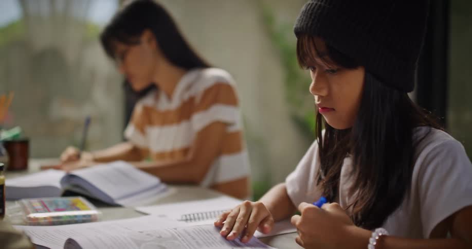 Two girls writing while opening textbook pages indoor at daytime