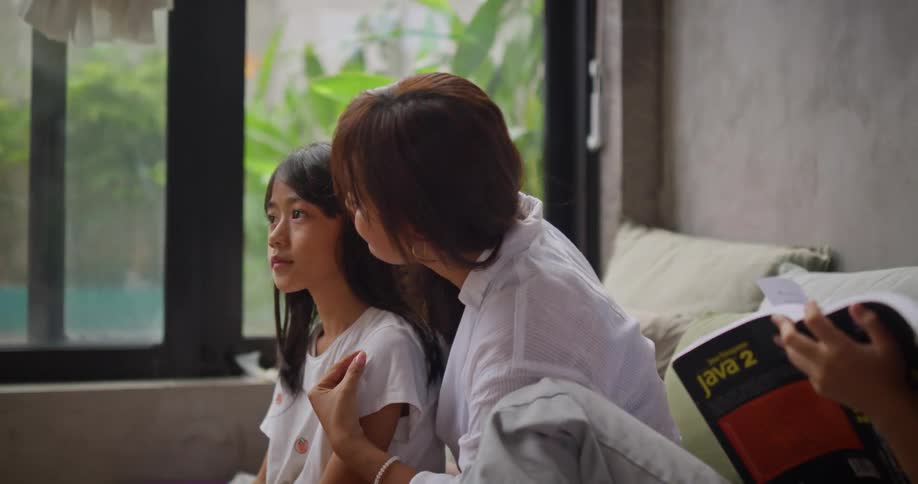 A mother is combing her daughters hair as her other daughter studies