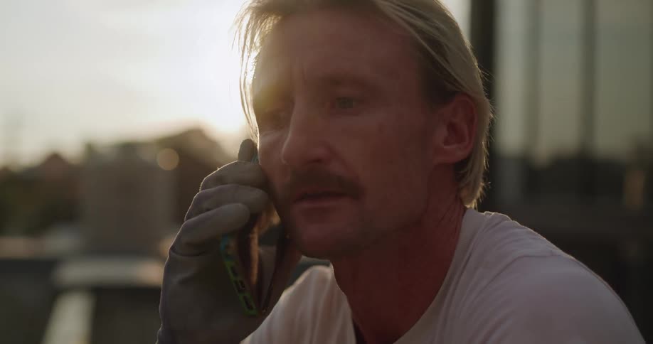 A construction worker pauses gardening on a rooftop to answer a phone call his expression turning thoughtful as he listens