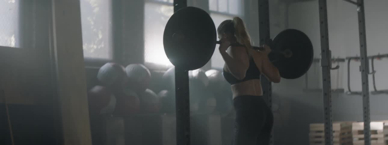 A woman puts a barbell on her shoulders and does squats