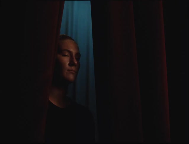 A woman peeks out from behind a curtain