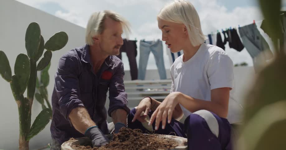A woman talks with a man digging in the dirt to put a plant in