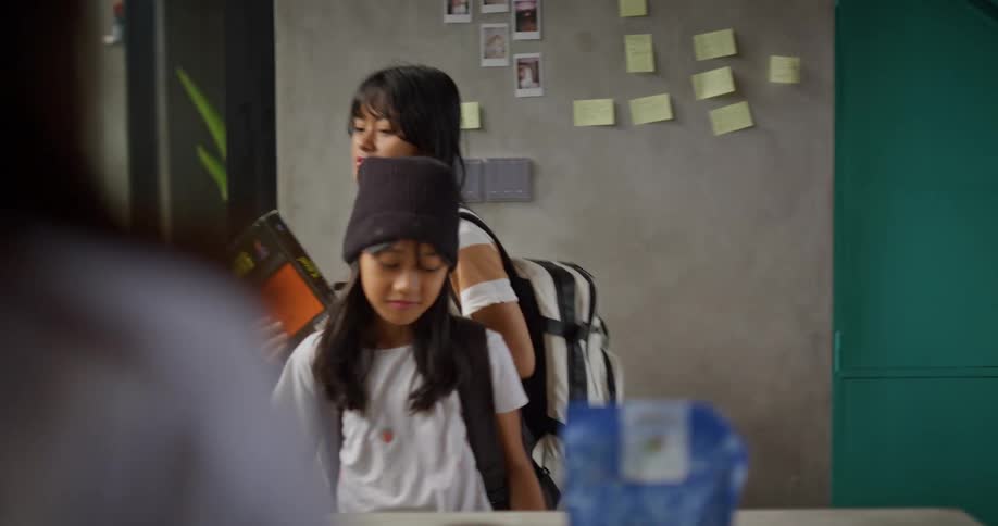 A child and a teenager arriving at school the teenager holding a book and placing it on a table