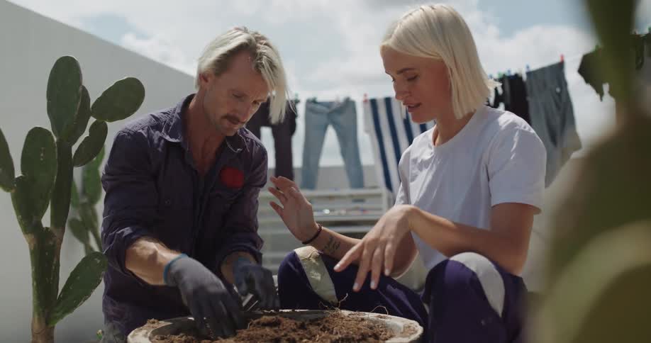 Man and woman on a balcony next to a potted plant with compost