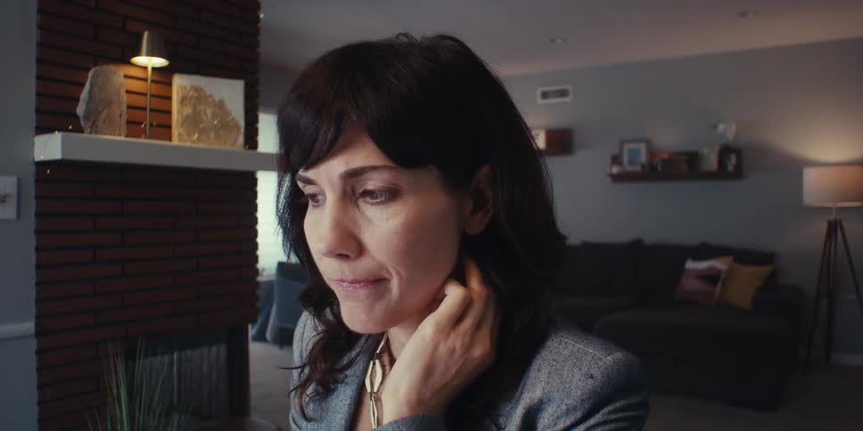 Woman sitting in a room of the house with a mix of emotions