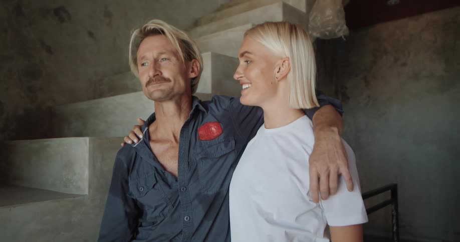 A man and woman hug and chat in an unfinished indoor space likely a home being renovated