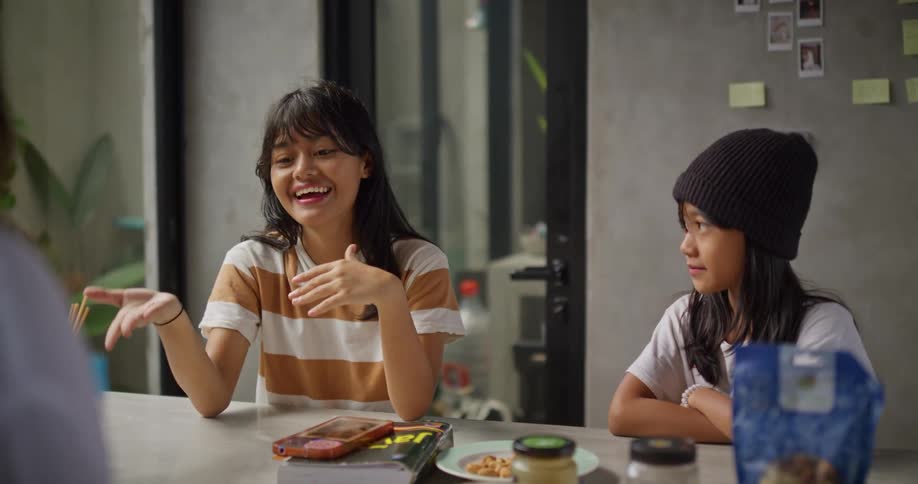 A teenager and a child sitting at a table talking with an adult woman and celebrating in a school setting