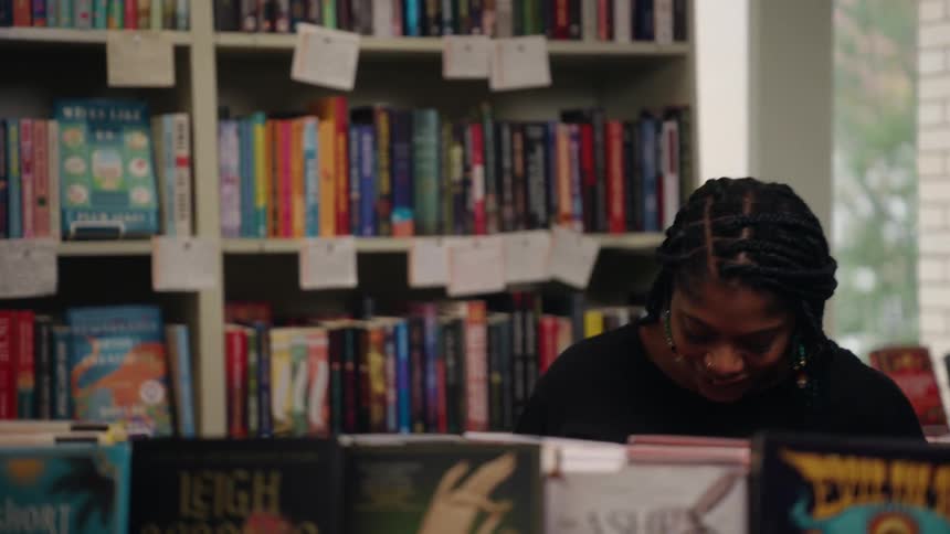 A smiling woman stands inside a cozy bookstore engaged in conversation surrounded by colorful books on neatly arranged shelves