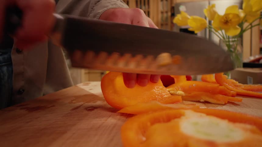 The woman is cutting orange and red peppers at home