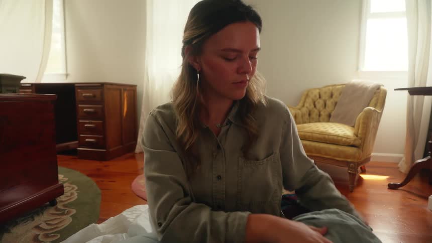 A woman is folding clothes and organizing them into a suitcase in a warmly lit bedroom