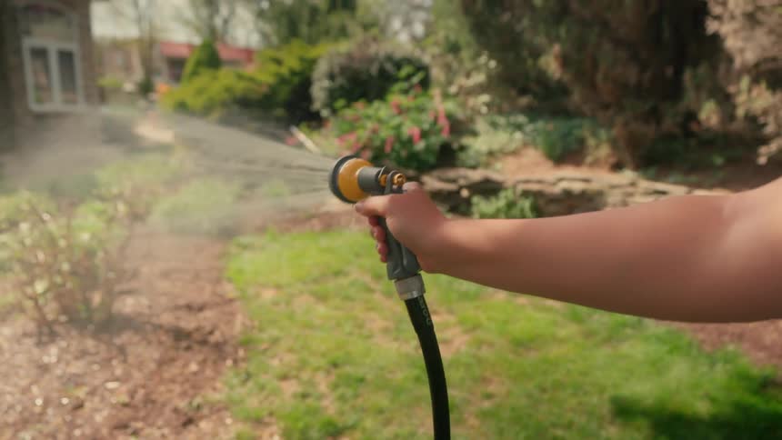 Hand of a lady watering plants in the yard during the day