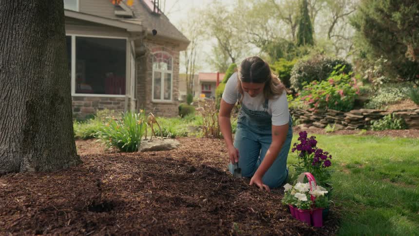 A woman digs in the soil to plant flowers in her yard