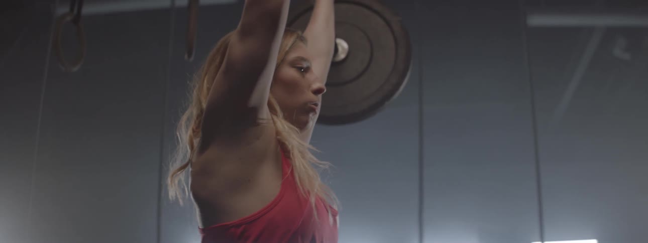 A woman lifts weights above her head then drops them