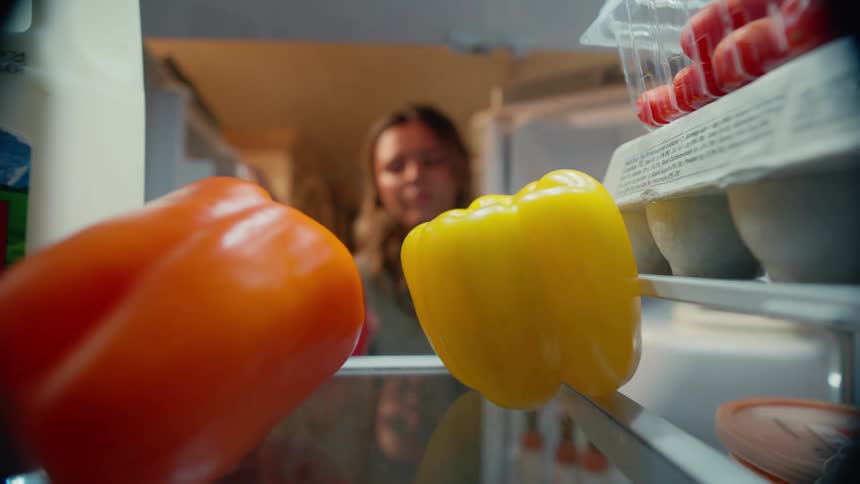 Point of view woman reaching into refrigerator pulling out red bell pepper from glass shelf