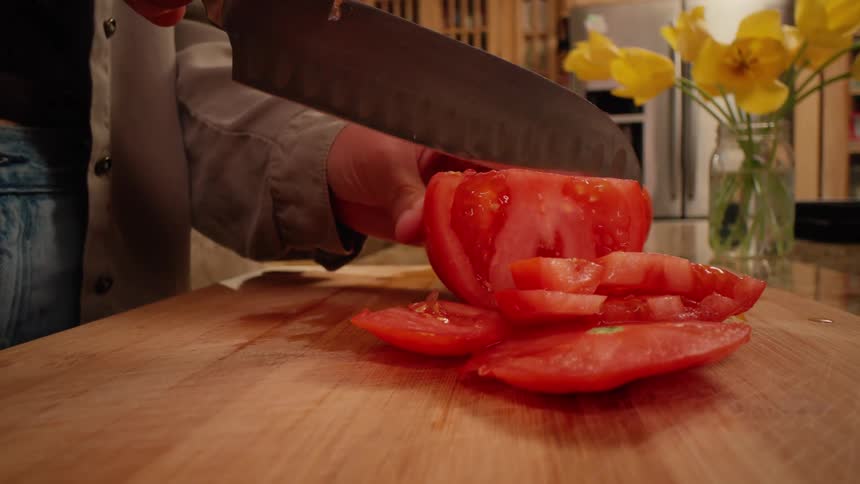 Pair of hands slicing tomatoes on a wooden board