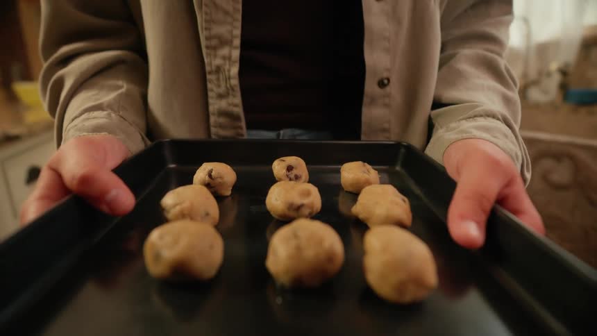 A woman carries a tray of cookie dough over to the oven